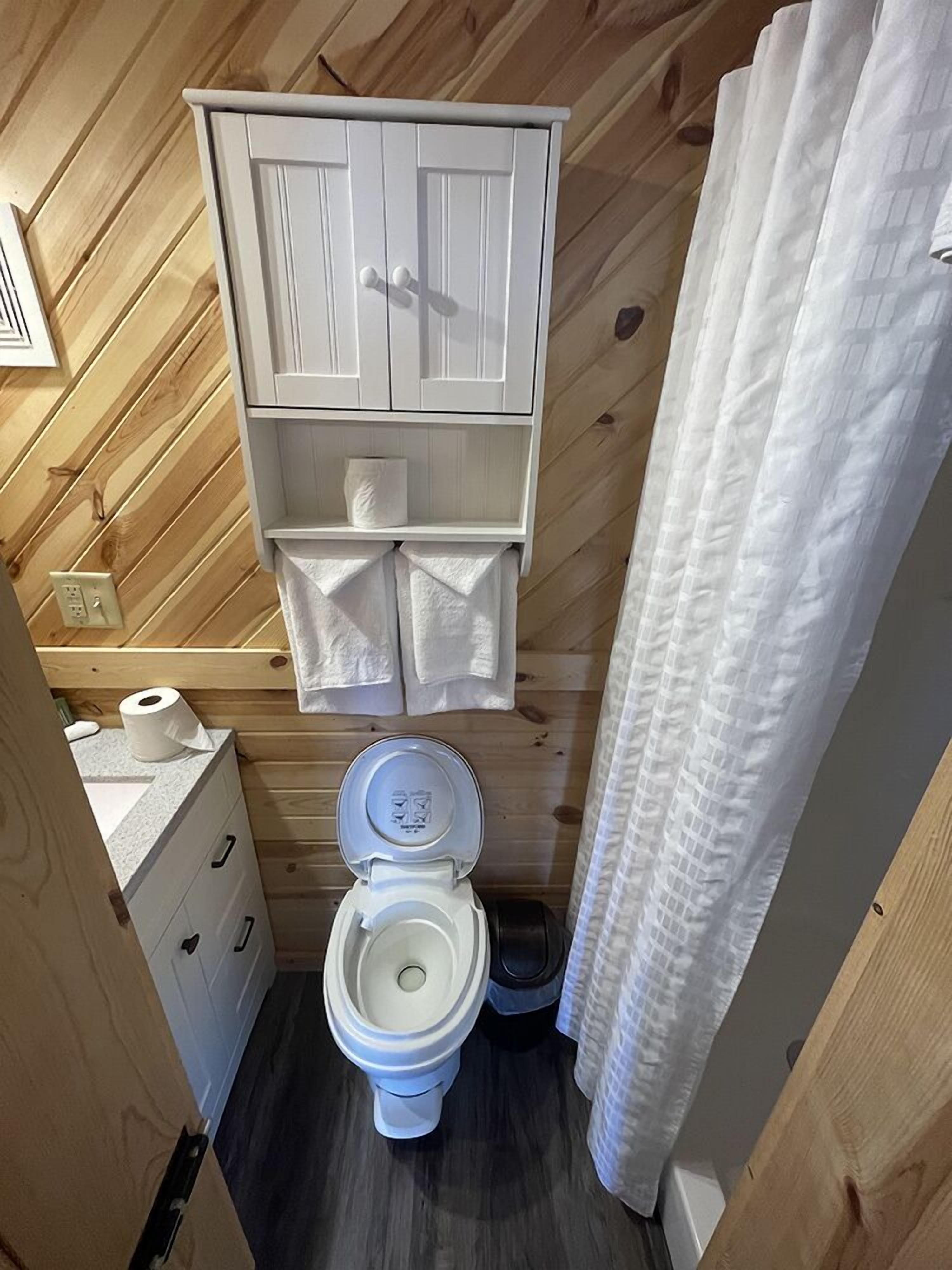 Een kleine badkamer met een houten plafond, een wit toilet, een klein kastje met een handdoekhouder en een douchegordijn.
