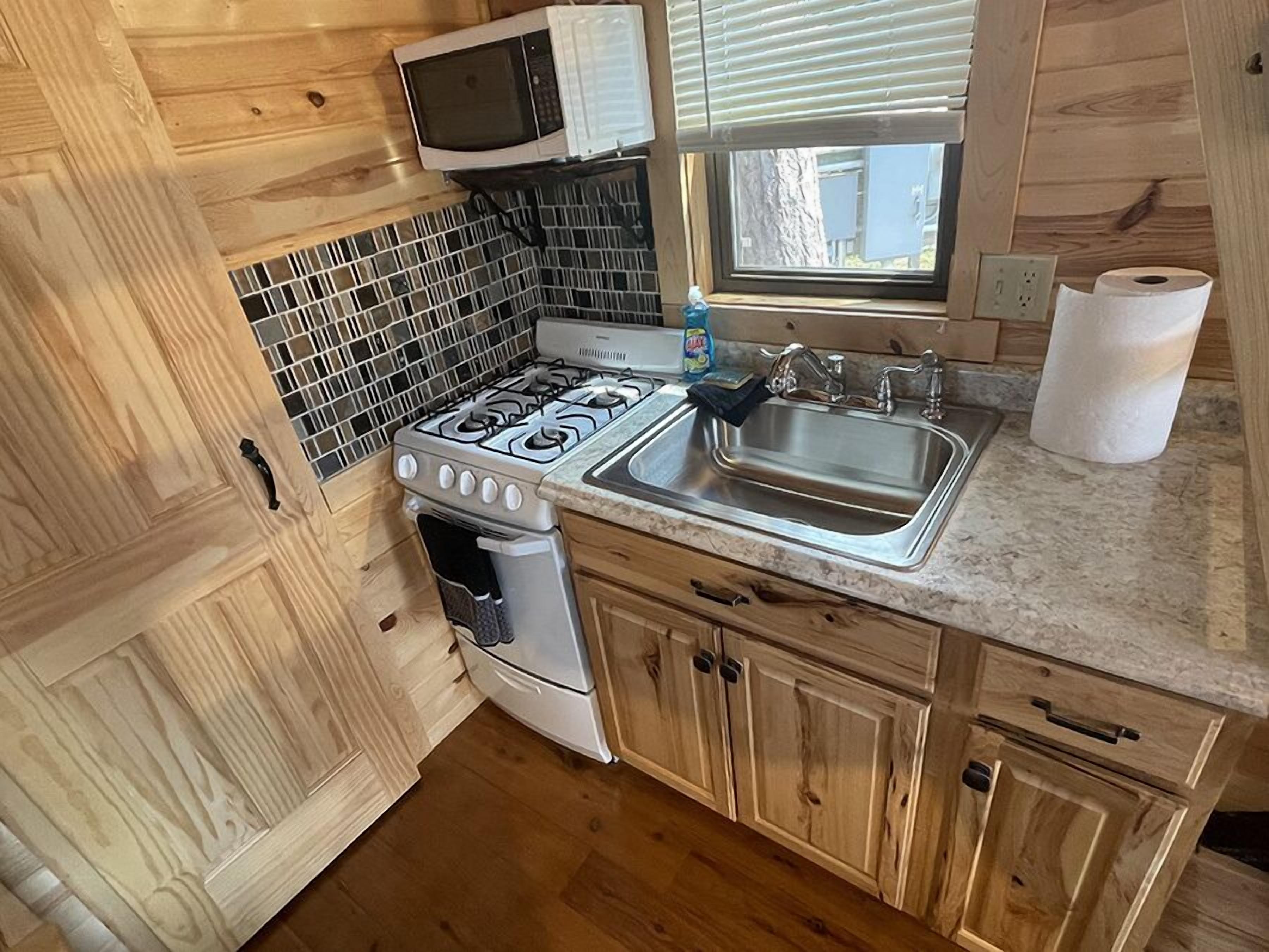 Cocina compacta con estufa a gas, microondas, pileta y muebles de madera.