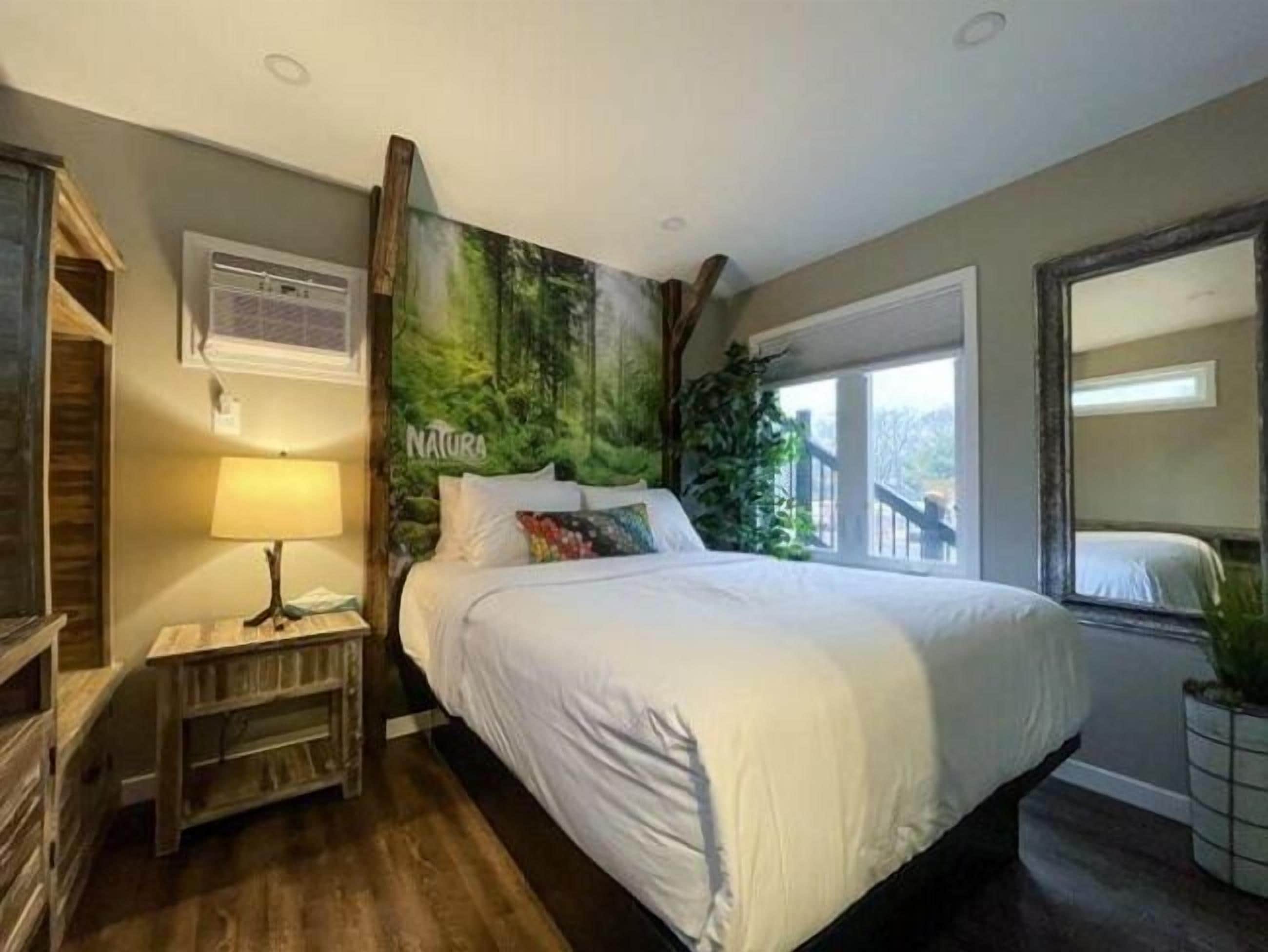Un dormitorio con una cama grande, una mesita de noche, una lámpara, una ventana con vistas y un aire acondicionado de pared.
