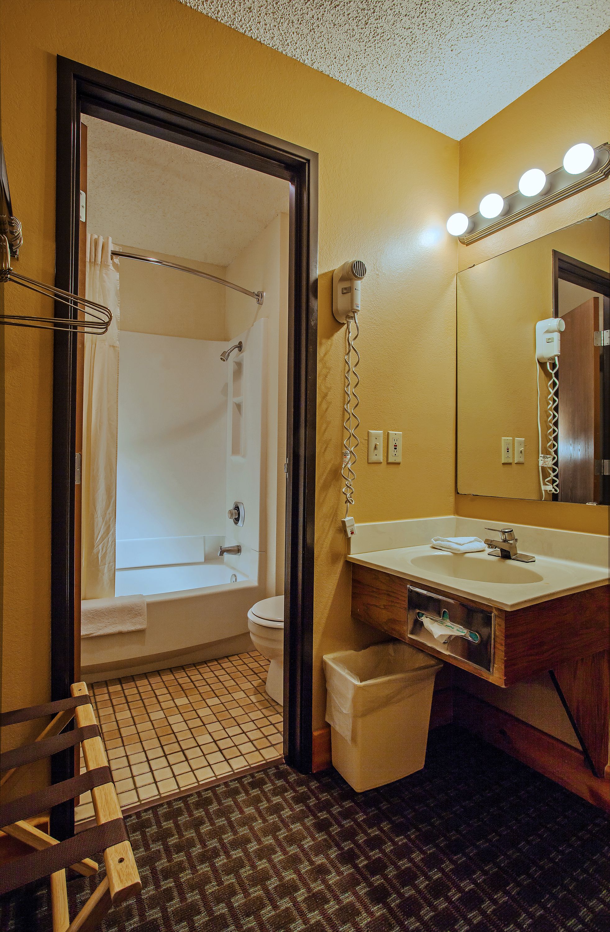 A bathroom with a bathtub, toilet, sink, and mirror with lights.