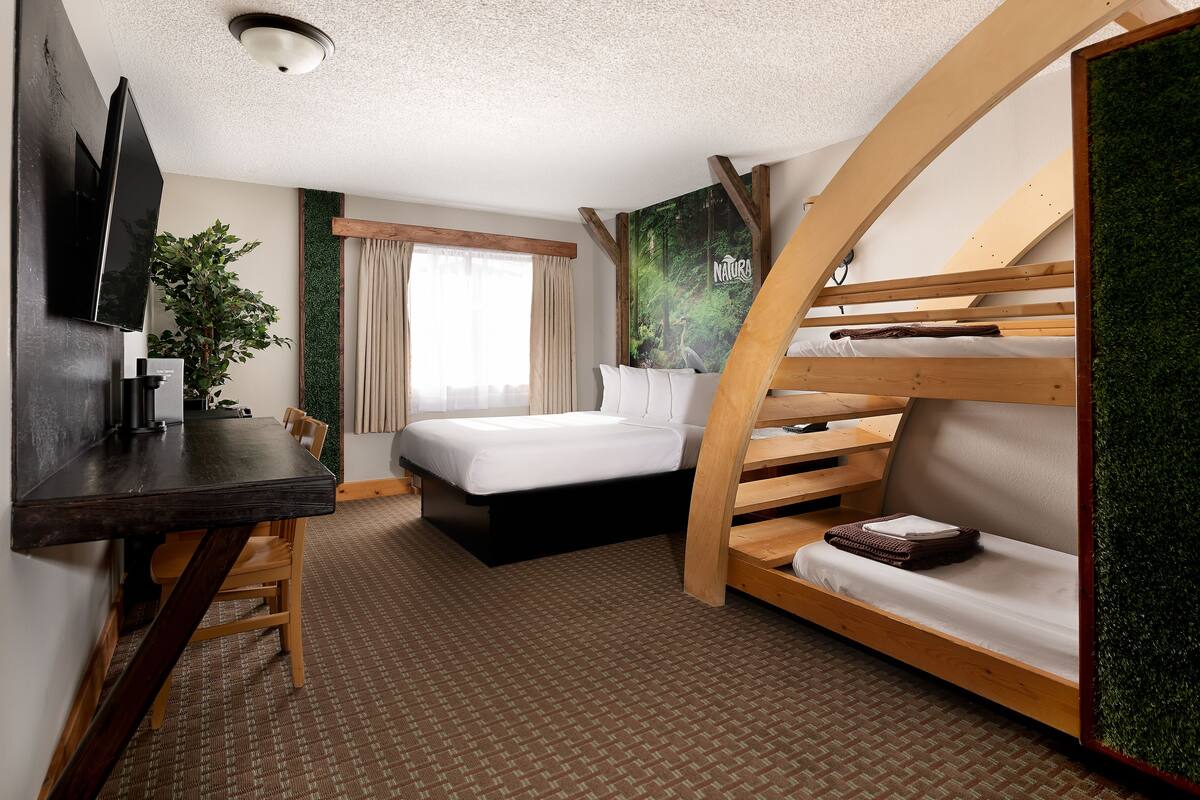 A hotel room with a bed, a desk, a chair, a TV, and a bunk bed.