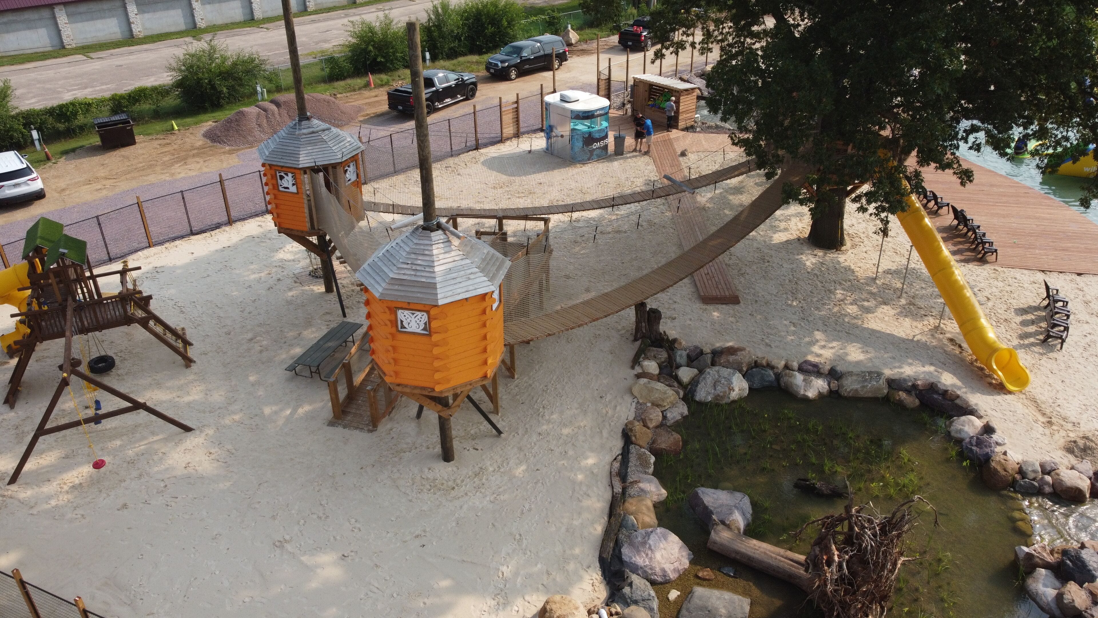 A playground with a rope bridge, sand play area, and a small water feature.