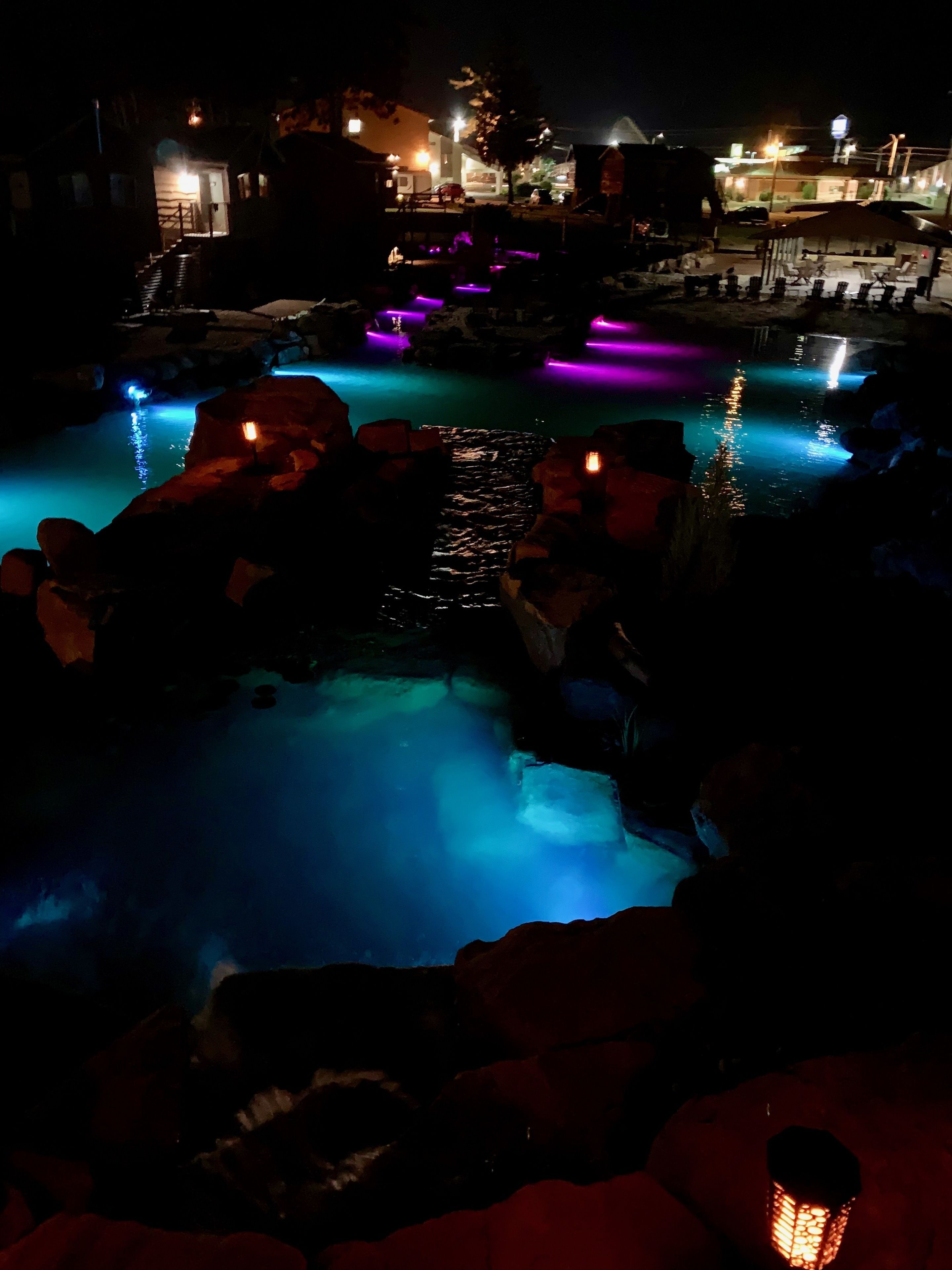 A nighttime view of a pool area with illuminated water features and surrounding structures.
