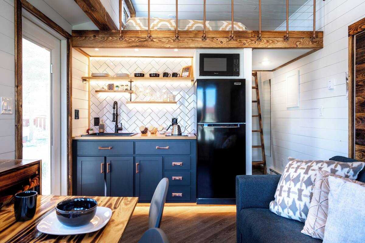 A compact kitchen with a microwave, refrigerator, and wooden ceiling.