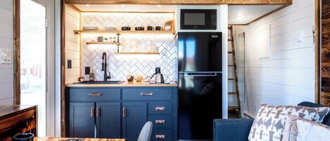 A compact kitchen with a microwave, refrigerator, and wooden ceiling.