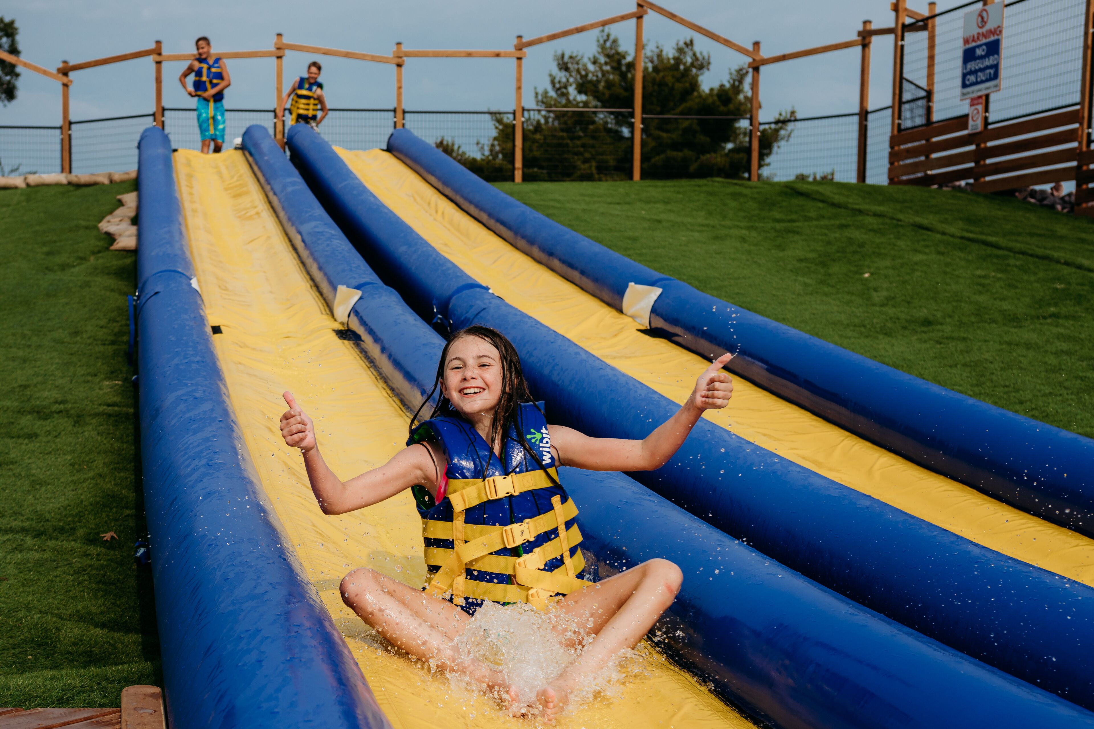 A person sliding down a water slide with blue and yellow sides, wearing a life jacket.