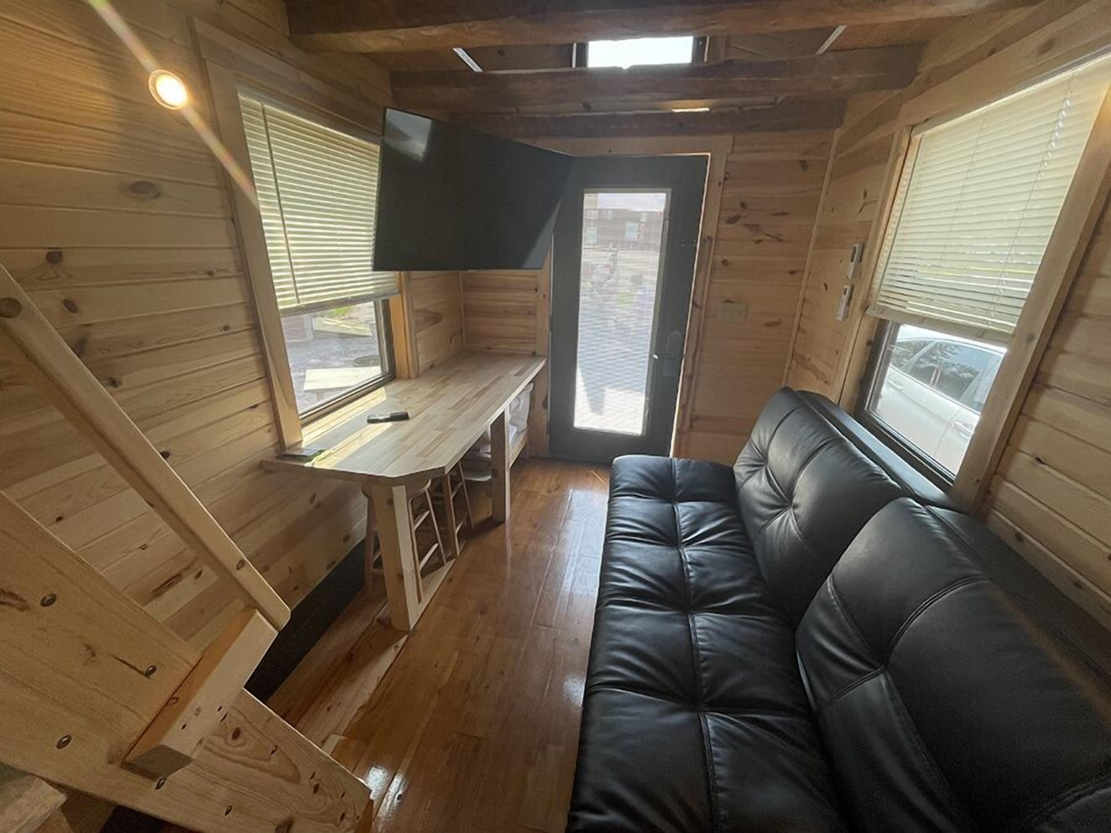 A compact cabin with a wooden interior, a black leather sofa, a small table, and a TV mounted on the wall.