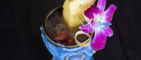 A cocktail with a pineapple and a purple orchid.