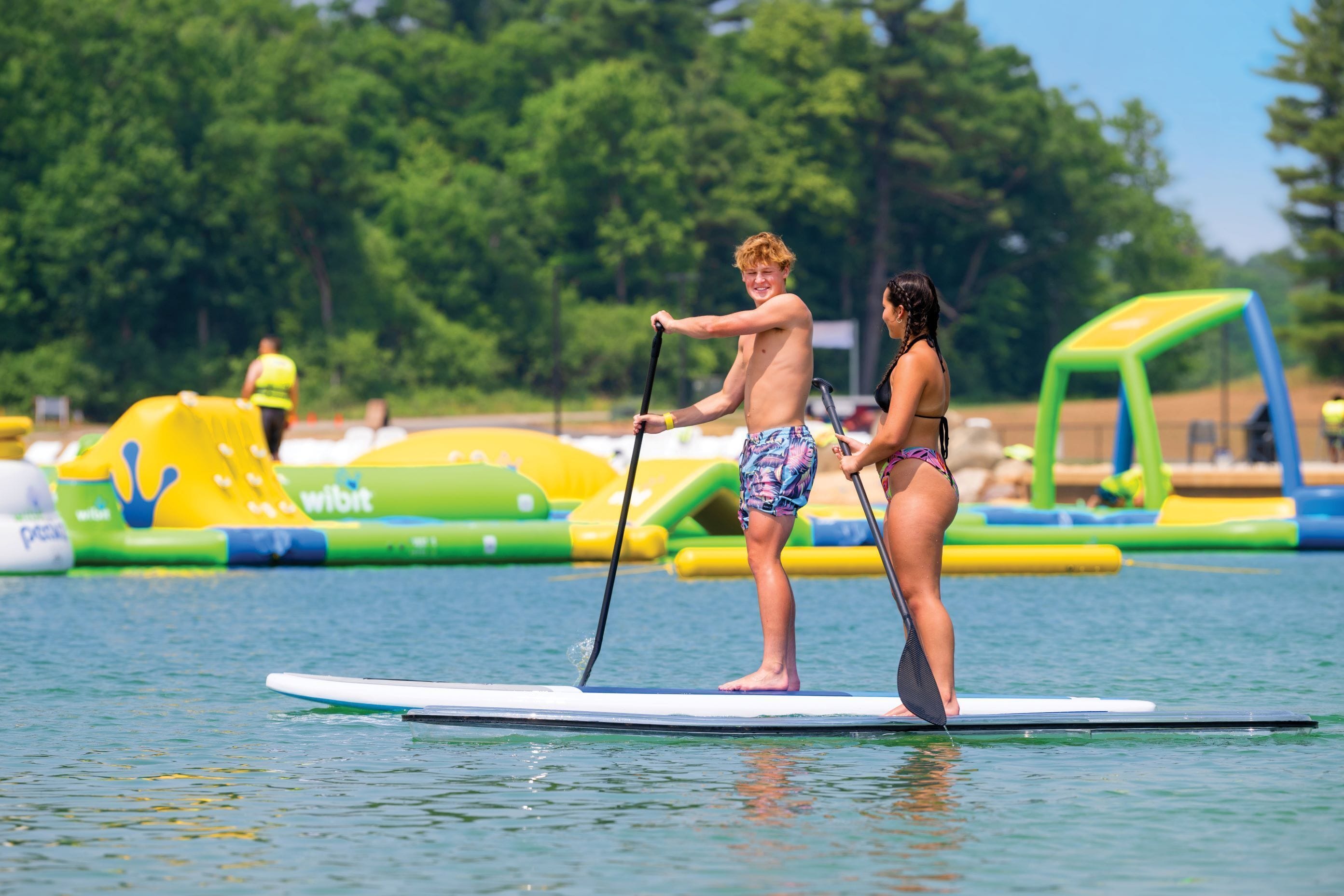 Two people on a paddleboard in a water body with inflatable structures in the background.