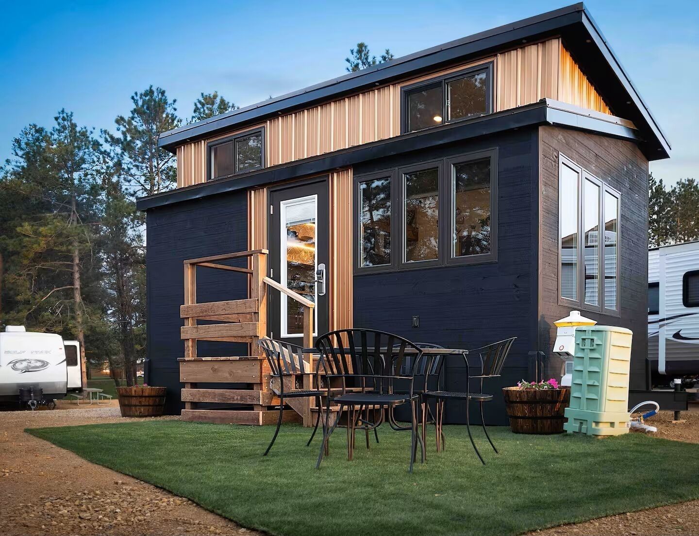 A modern two-story building with a wooden exterior, large windows, and a patio with outdoor furniture.