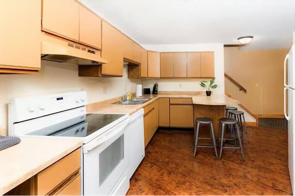 A kitchen with wooden cabinets, a white stove, a sink, and a bar stool area.