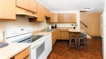 A kitchen with wooden cabinets, a white stove, a sink, and a bar stool area.