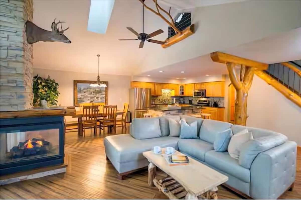 A cozy living room with a fireplace, a sofa, a dining area, and a kitchen.