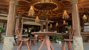 A rustic wooden interior with a central table, chairs, and hanging light fixtures.