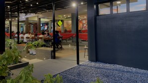 An indoor dining area with tables and chairs, potted plants, and a view of the sky through large windows.