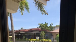 A view through a window of a building with a gravel driveway, palm trees, and a sign indicating a restaurant.