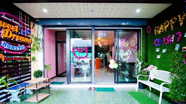 A hotel entrance with a neon sign, glass doors, indoor seating, and a green wall with decorations. - Sweet Dreams Hometel (Krabi)