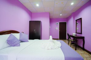 Una habitación con paredes moradas, una cama con ropa de cama blanca y almohadas moradas, un armario de madera, un escritorio con una silla y un espejo en la pared.