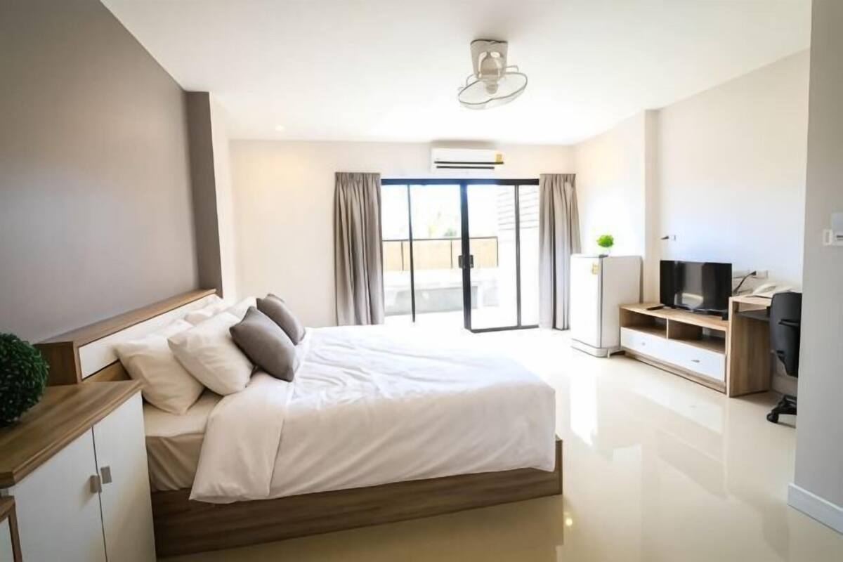 A modern hotel room with a large bed, a television, a desk, and a sliding glass door to the outside.