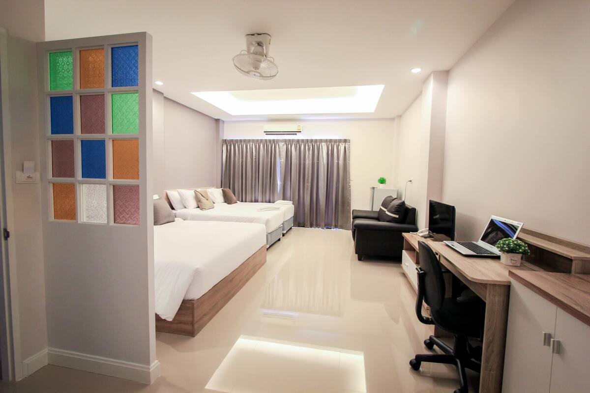 A modern hotel room with a large bed, a desk with a laptop, a chair, and a small plant.