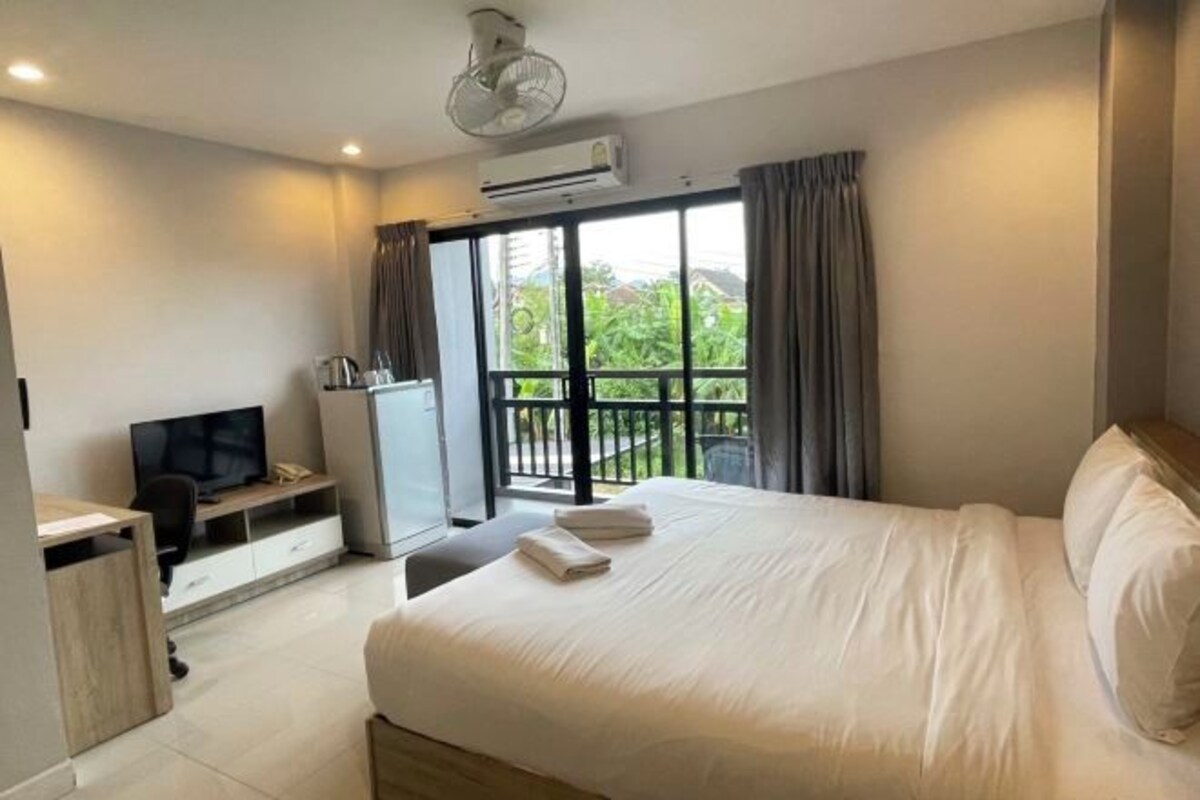 A hotel room with a large bed, a desk with a TV, a minibar, and a balcony with curtains.