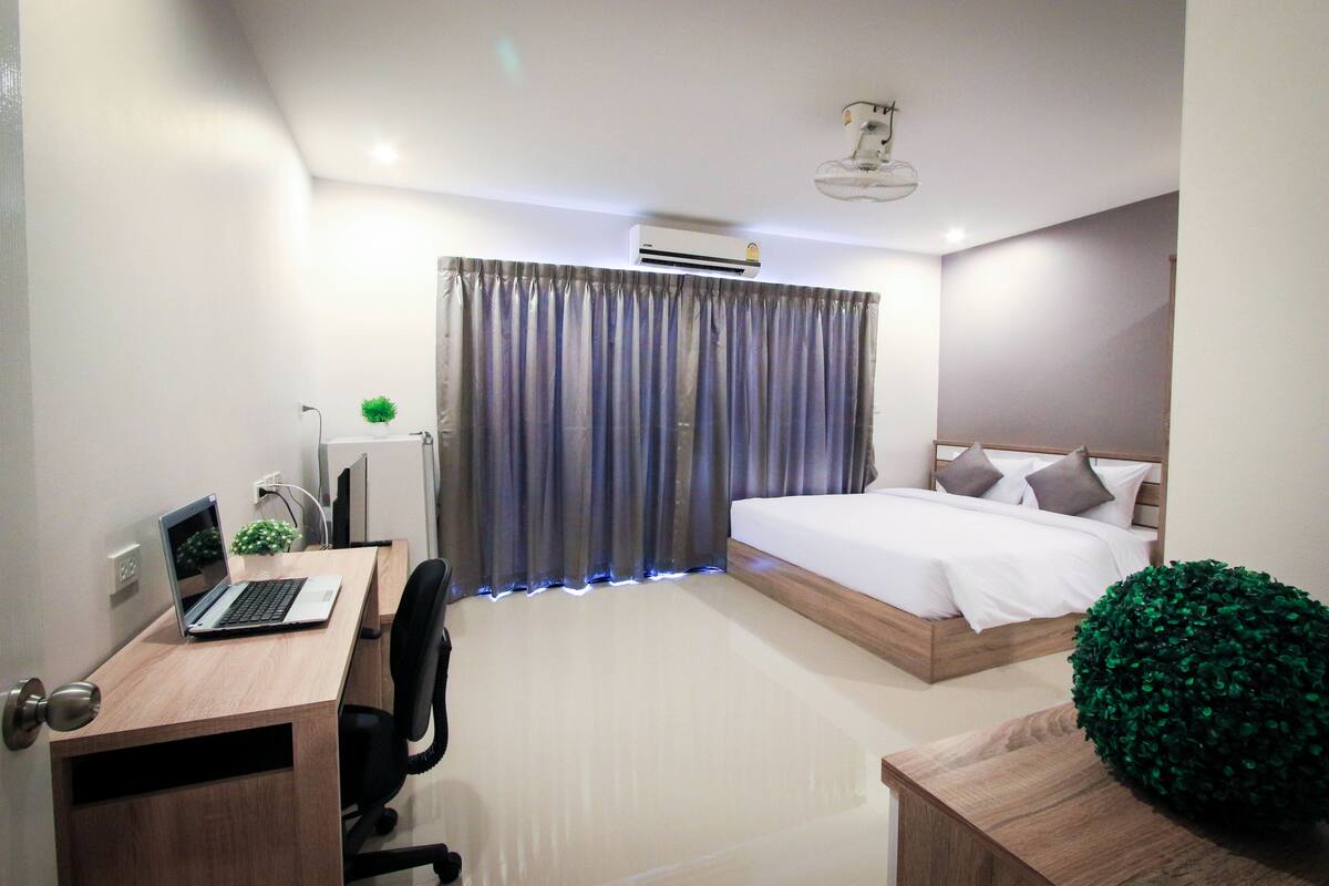 A modern hotel room with a wooden desk, laptop, and a bed with white bedding.