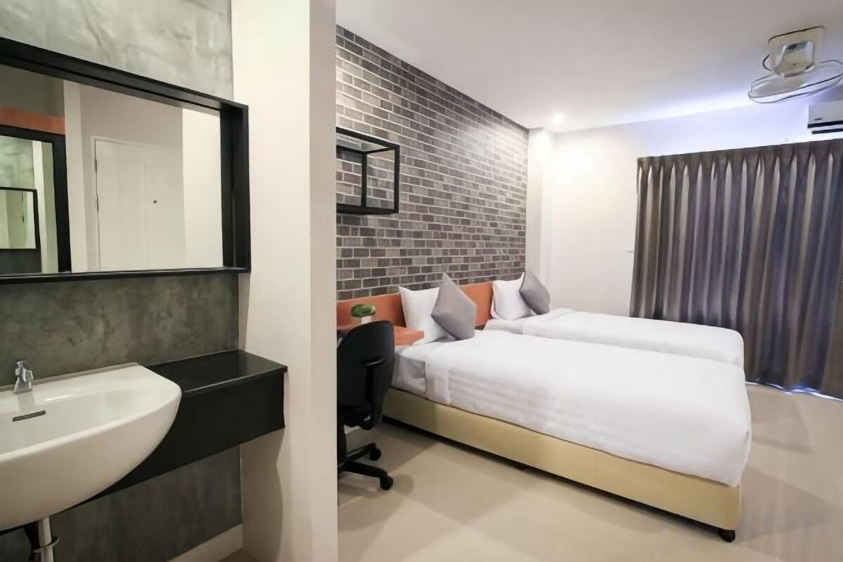 A modern hotel room with a large bed, a bedside table, a chair, a large mirror, and a bathroom with a sink.