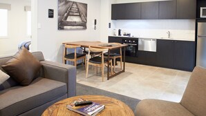 A modern kitchen with dark cabinets, a dining area with a wooden table and chairs, and a living area with a sofa and a coffee table. - Kelly Rd Cambridge Lodge (Cambridge)