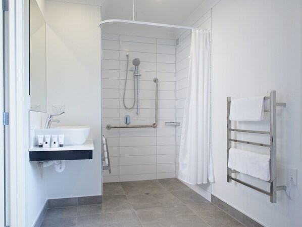 Un baño moderno con ducha, barras de apoyo, toallero y lavamanos con artículos de aseo.
