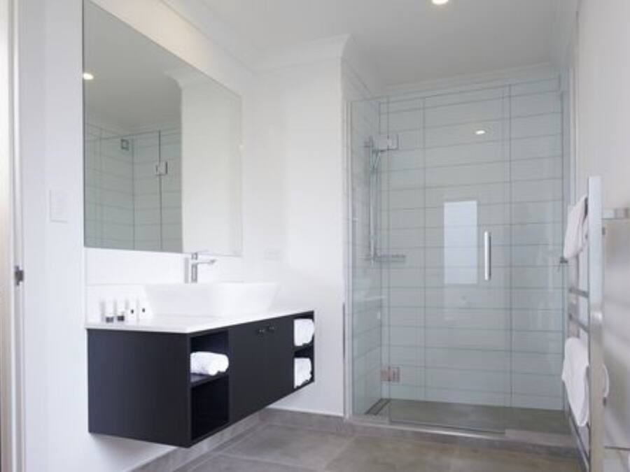 Un baño moderno con cabina de ducha de vidrio, lavamanos blanco y tocador negro.
