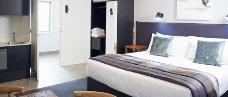 Una habitación de hotel moderna con una cama grande, una mesa de comedor de madera, una zona de cocina y un baño.