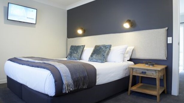 A modern bedroom with a large bed, two wall-mounted lights, and a small wooden nightstand. - Kelly Rd Cambridge Lodge (Cambridge)