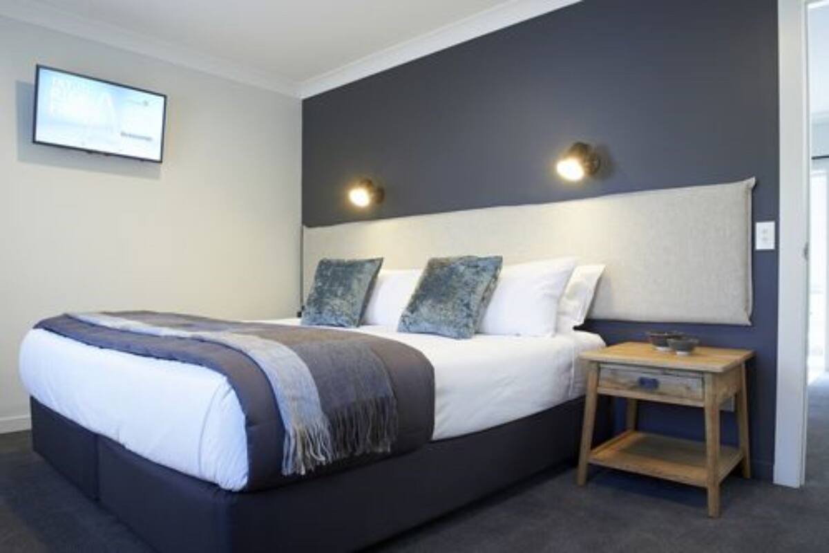 A modern bedroom with a large bed, two wall-mounted lights, and a small wooden nightstand.