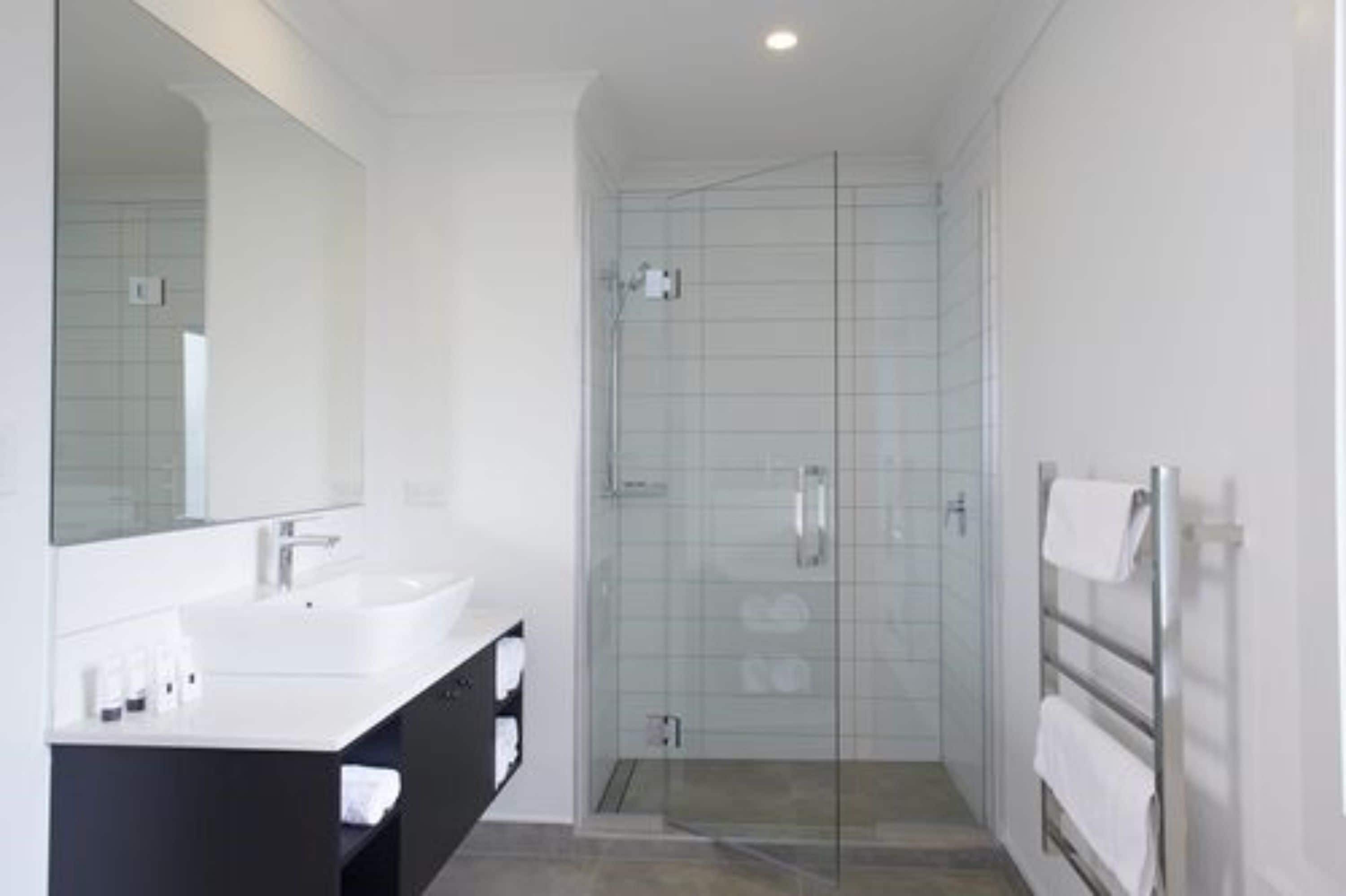A modern bathroom with a large mirror, two sinks, a shower enclosure, and a towel rack.