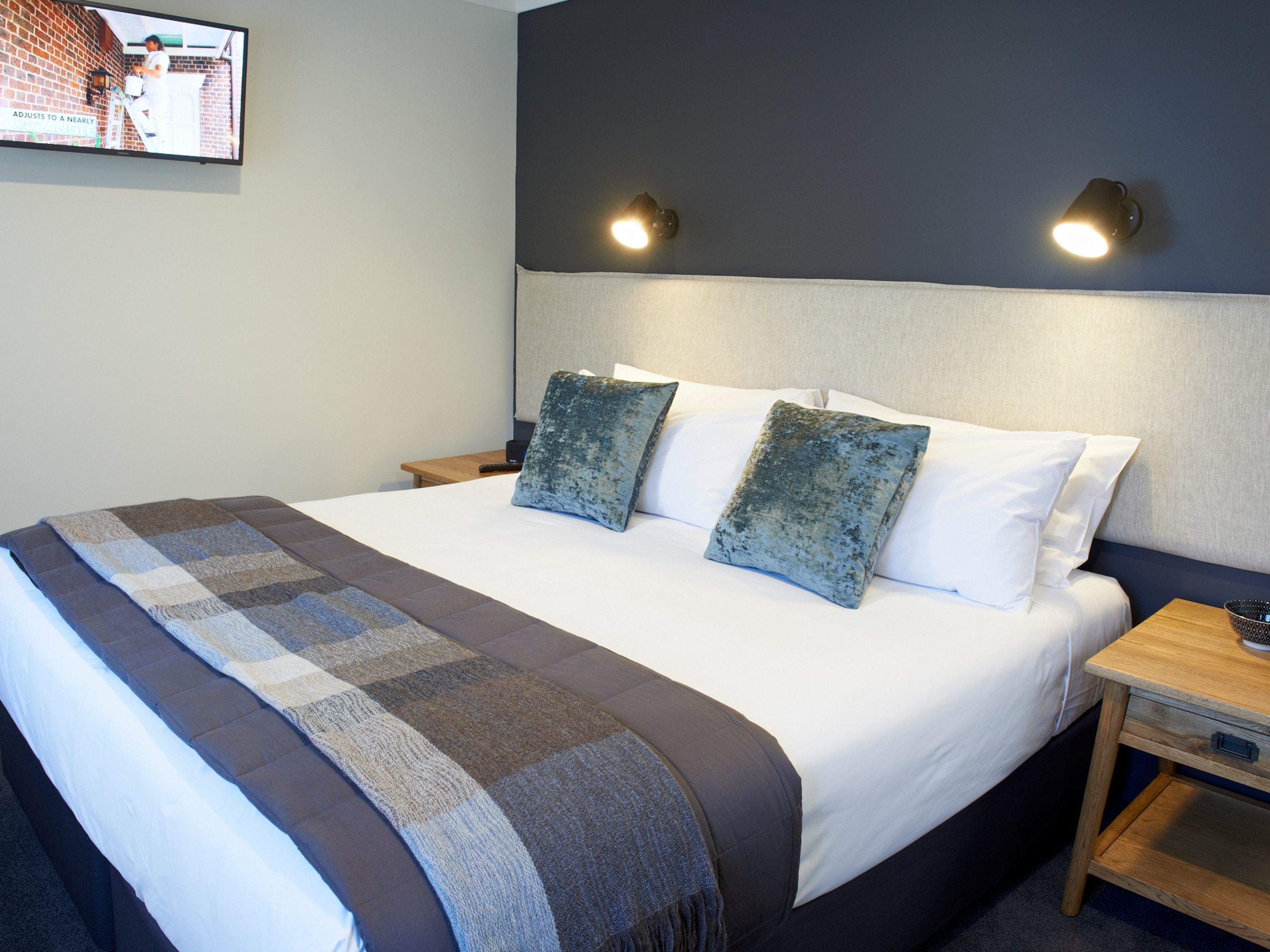 A neatly made bed with a checkered blanket, two pillows, and a bedside table with a lamp.