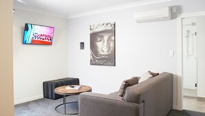 A modern living room with a grey sofa, a wooden coffee table, a black ottoman, and a TV mounted on the wall. - Kelly Rd Cambridge Lodge (Cambridge)