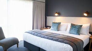 A modern hotel room with a large bed, a chair, a nightstand, and a lamp. - Kelly Rd Cambridge Lodge (Cambridge)