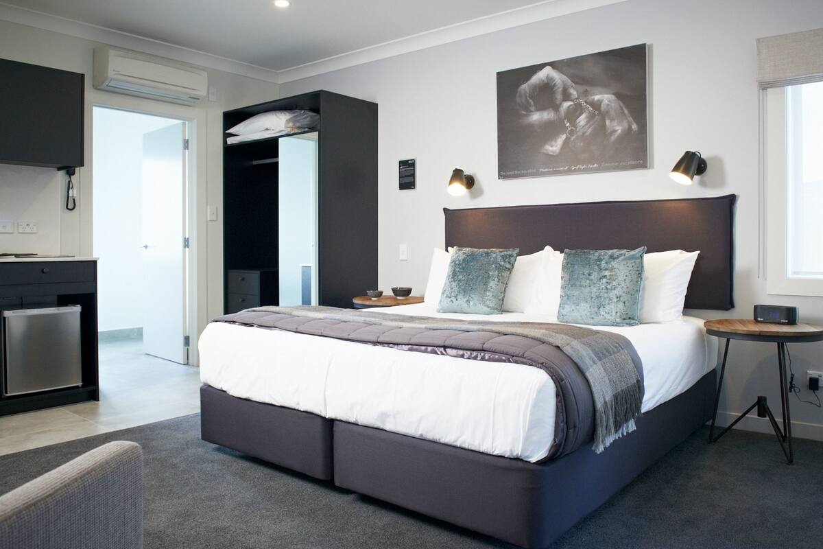 A modern bedroom with a large bed, a small bedside table, a nightstand, and a wall-mounted lamp.