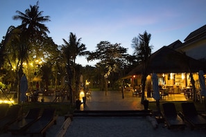 A beachfront resort with lounge chairs, a bar, and palm trees.