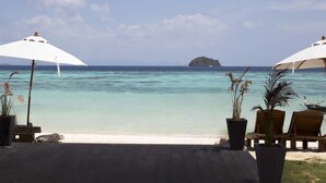 A beachside patio with two white umbrellas, potted plants, and wooden chairs facing a clear blue sea with a small island in the distance. - Mali Resort Sunrise Beach (Koh Lipe)