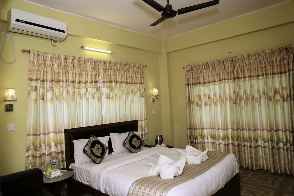 Quarto de hotel com cama, cortinas, ventoinha no teto e ar condicionado.