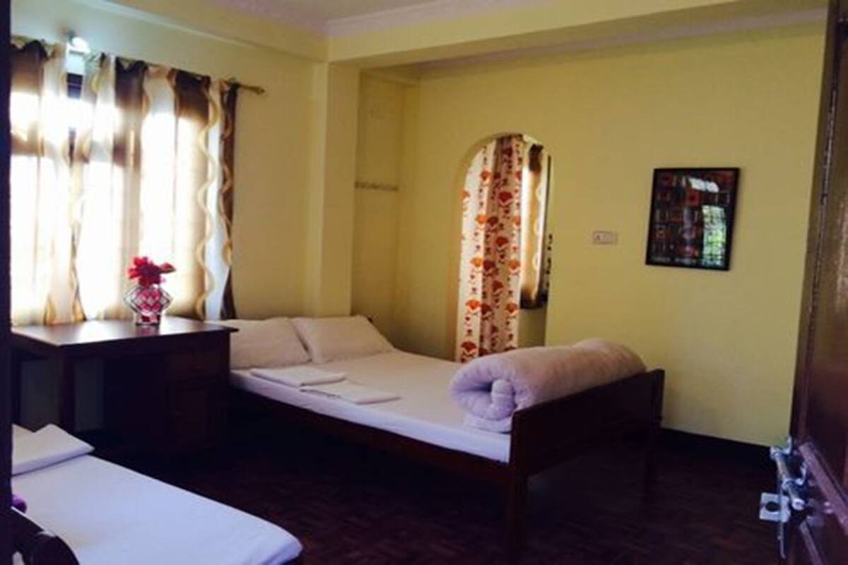 A single bed with a wooden frame, a bedside table with a vase, and a window with curtains.