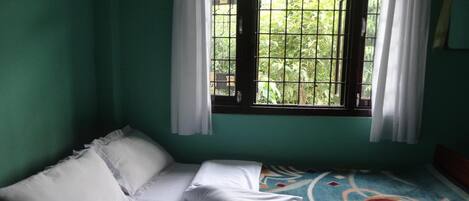 Una habitación con cama, ventana con barrotes y vista a follaje exterior.