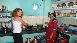 Una cocina con dos personas cocinando, ollas de cobre, una estufa a gas y estantes con utensilios de cocina.