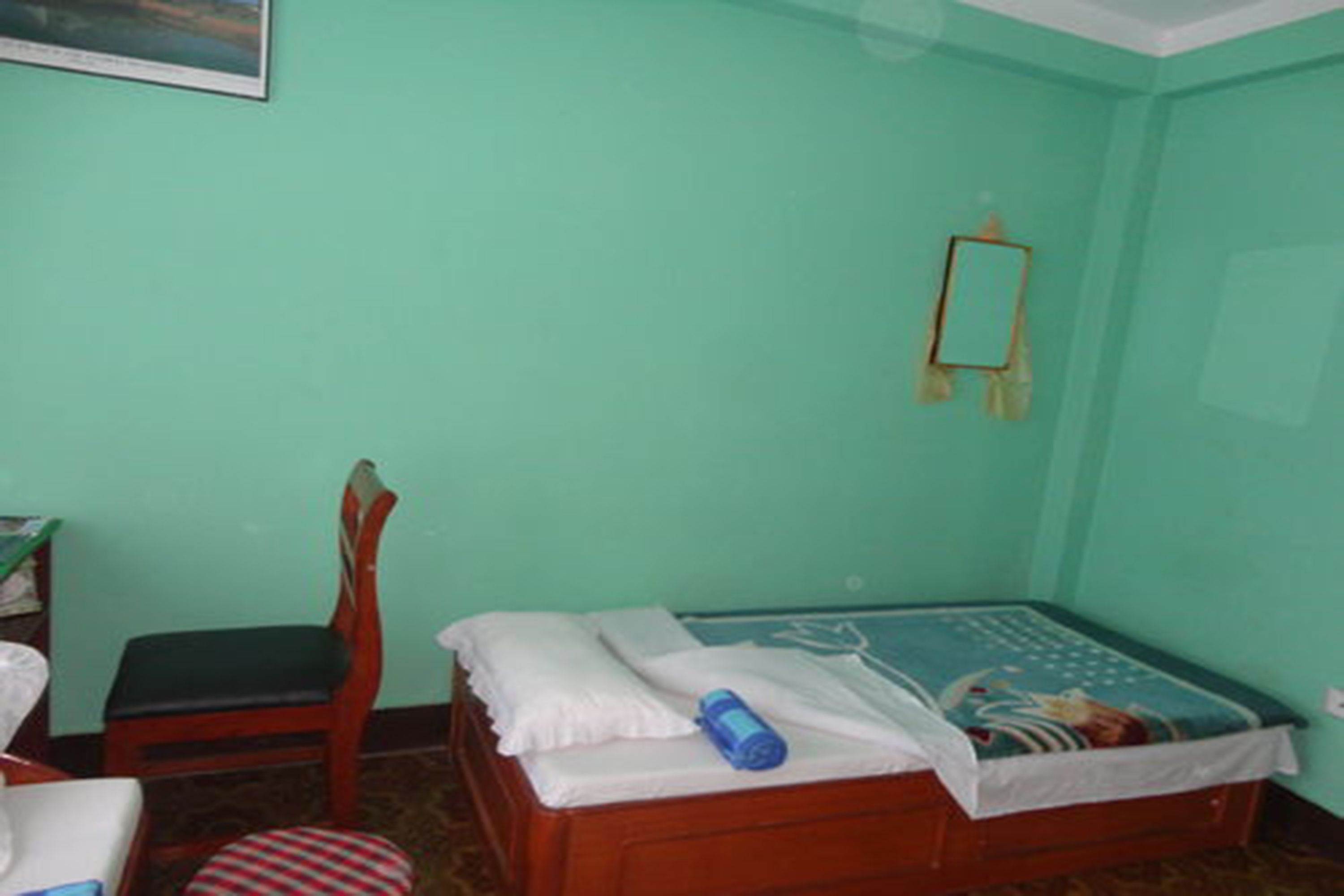 Une petite pièce avec un lit, une chaise, un bureau et un miroir au mur.