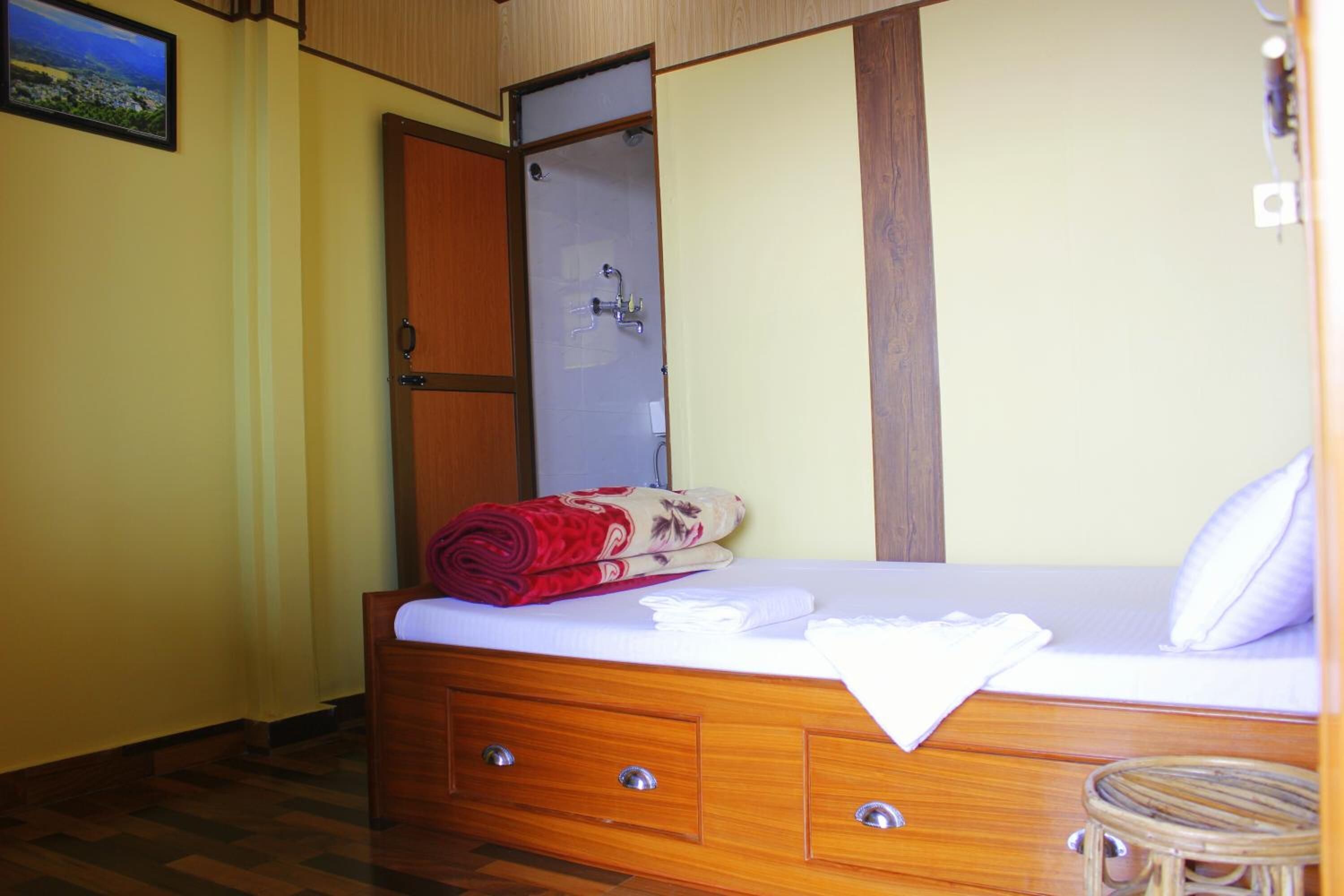 A bedroom with a wooden bed, a small bedside table, a mirror, and a door leading to a bathroom.