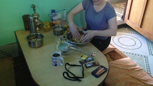 Una persona sentada en una mesa con varios objetos, entre ellos un bol, una taza y algunos productos envasados.