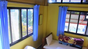 Una habitación pequeña con cama individual, ventana, cortinas y una colcha estampada.