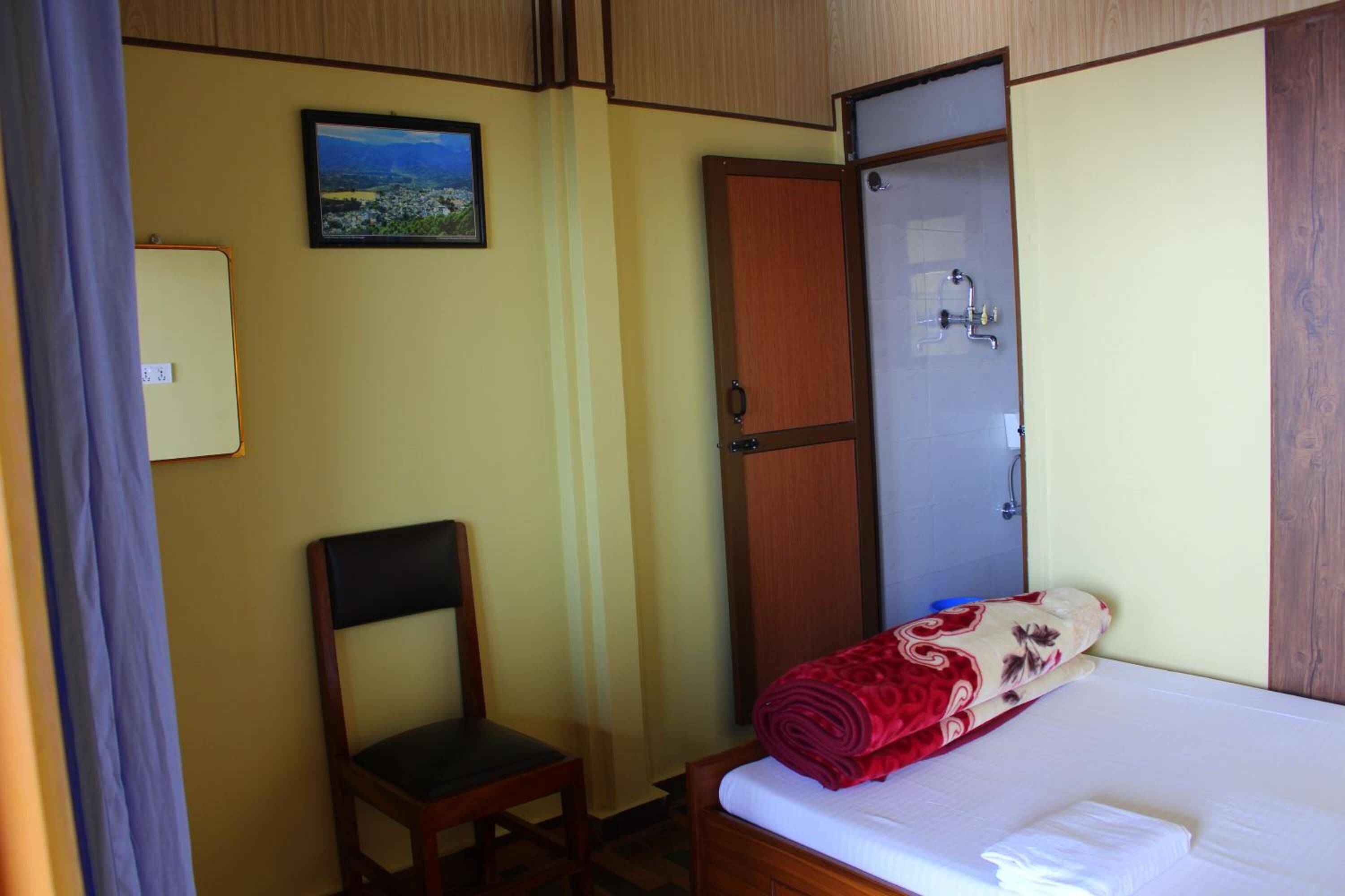 Una habitación de hotel con cama, una silla, armario y ducha.