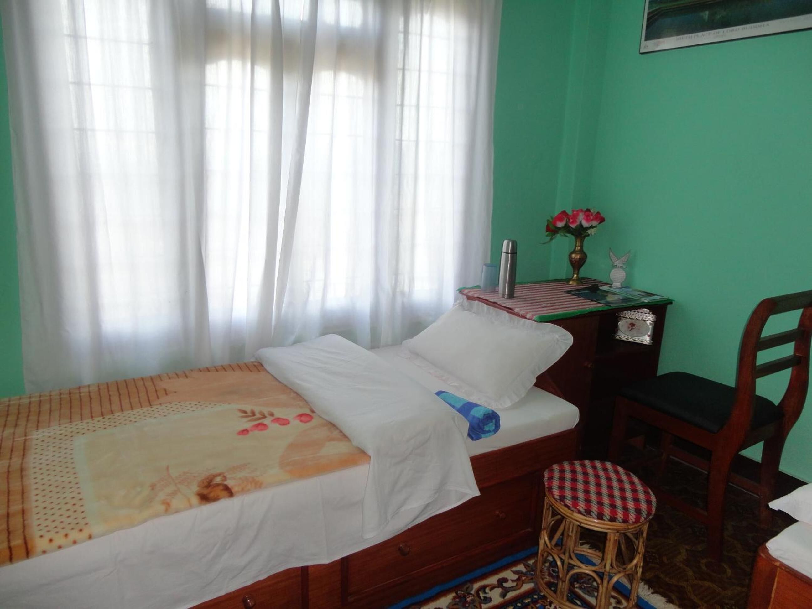 Una cama pequeña y ordenada con una colcha estampada con motivos florales, una mesita de noche con un florero y una silla.